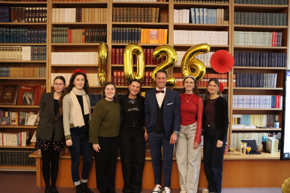 Die Azubis posieren zusammen mit dem Geschäftsführer vor einem Bücherregal beim Neujahrsempfang
