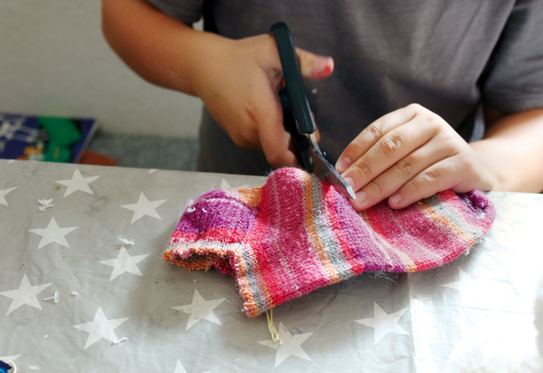 Eine bunte Socke zerschneiden, um daraus Mützen und Schals zu fertigen.
