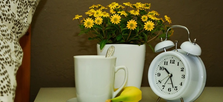 Ein Nachttisch mit einer Tasse, Blumen und einem Wecker