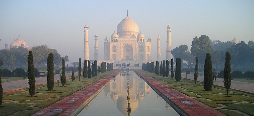 Es ist das Mausoleum Taj Mahal zu sehen. Ein weißes Gebäude mit Kuppeln und kunstvoll verzierten Elementen.