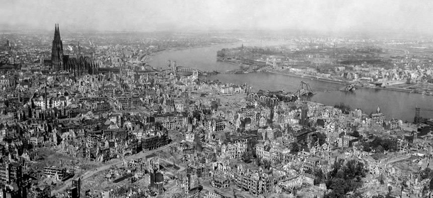 Es ist ein schwarzweiß Bild aus Vogelperspektive einer zerbombten Stadt zu sehen.