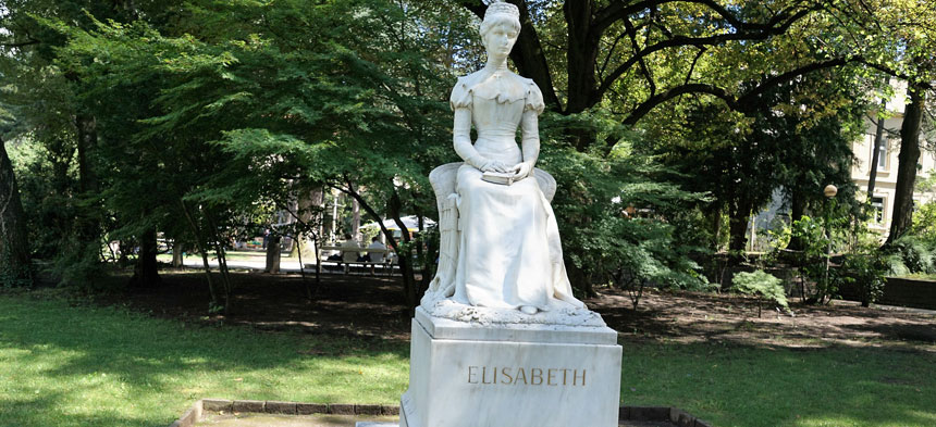 Das Denkmal aus weißen Marmor besteht aus einem quadratischen Sockel, auf dem eine Frau mit Kleid sitzt.