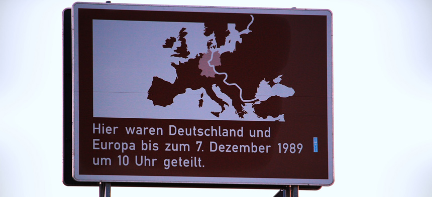 Es ist ein braunes Verkehrsschild mit der Aufschrift "Hier waren Deutschland und Europa bis zum 07. Dezember 1989 um 10 Uhr geteilt.