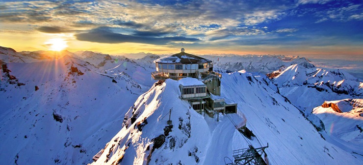 Es ist ein Schneebedecker Berg zu sehen, das Schilthorn, mit einem runden Haus auf dem Gipfel.