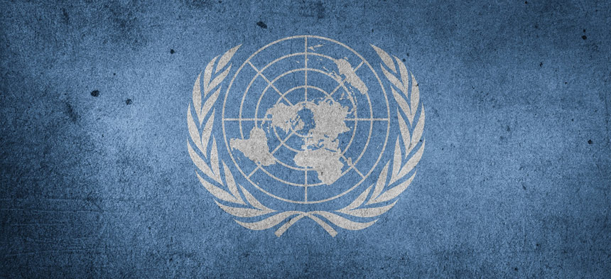 Das blaue Logo der Vereinten Nationen ist zu sehen:  Die Welt ist vom Nordpol aus zu sehen, die Erdkugel wird von einem Lorbeerkranz umrandet. 
