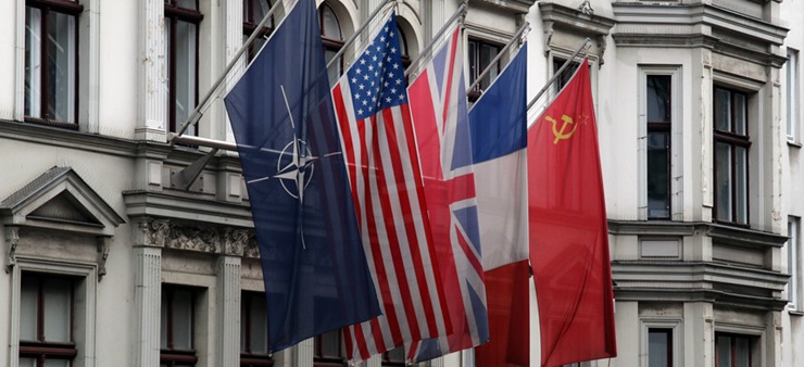 An einem weißen Gebäude hängen die Flagge von der NATO, USA, UK, Frankreich und Sowjetunion.