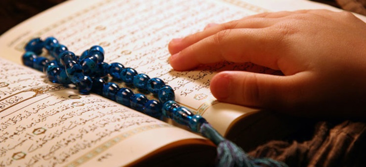 Auf einem aufgeschlagenen Koran liegt eine Kette mit blauen Perlen.