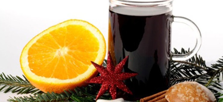 Auf einem Tannenzweig liegt eine orange, eine Tasse Glühwein und Gebäck.