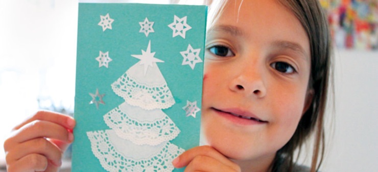 Mädchen hält türkise selbstgebastelte Weihnachtskarte in die Luft.