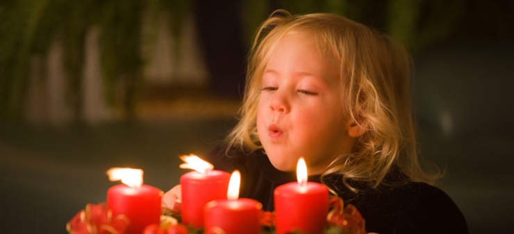 Kind pustet vier rote Kerzen auf einem Adventskranz aus