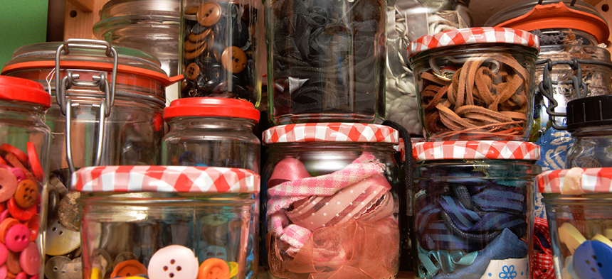 Eine Vielzahl an Einmachgläsern, die gefüllt sich mit unterschiedlichsten Materialien wie Gummibänder, Knöpfe und Tücher.