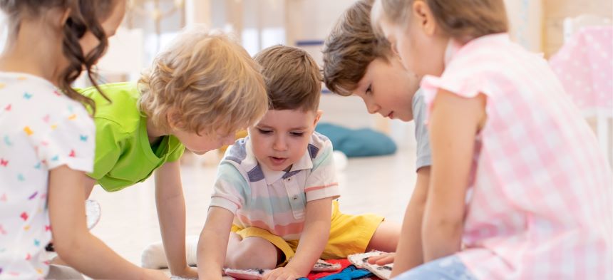 Fünf Kinder bilden einen Sitzkreis und beschäftigen sich angeregt mit nicht sichtbaren Spielgegenständen.