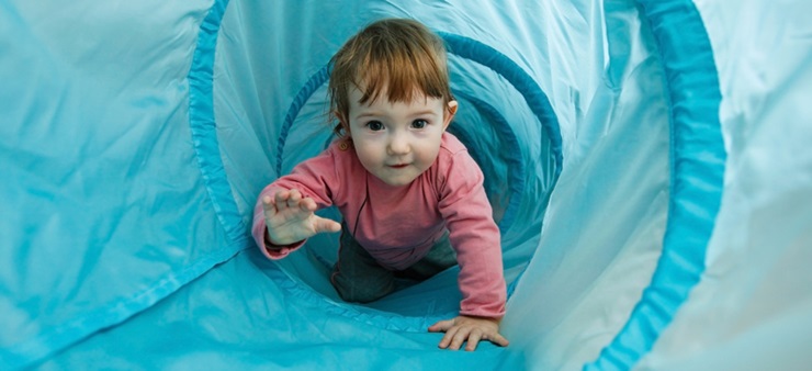 Kleine Junge krabbelt glücklich durch einen hellblauen Tunnel
