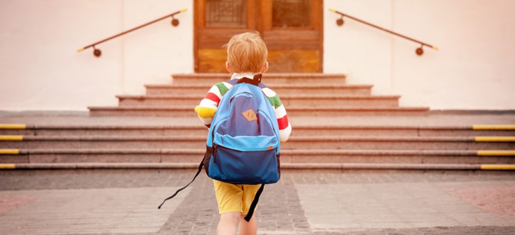 Kleiner Junge mit Rucksack geht auf Eingang zu.