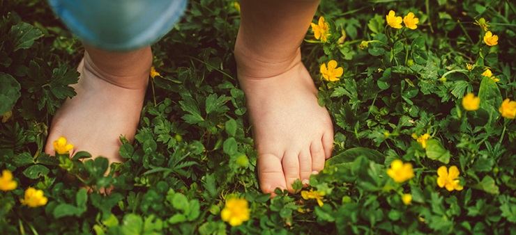 Auf einer dunkelgrünen Wiese mit gelben Blüten stehen zwei Kinderfüße und fühlen das Gras.