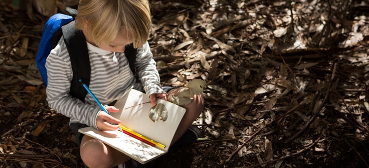 Kind mit blauem Rucksack malt in ein Notizbuch
