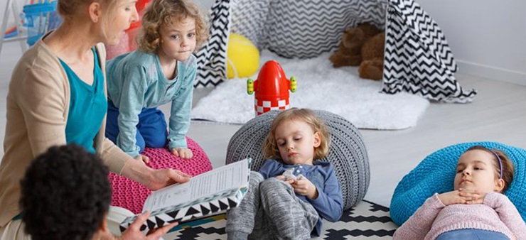 Frau liest Kindern auf schwarz-weißem Teppich eine Geschichte vor.