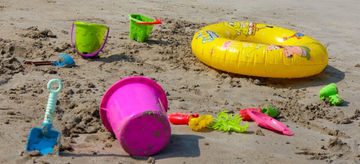 Eimer, Schaufeln und ein aufblasbarer Schwimmring liegen verteilt im Sand.