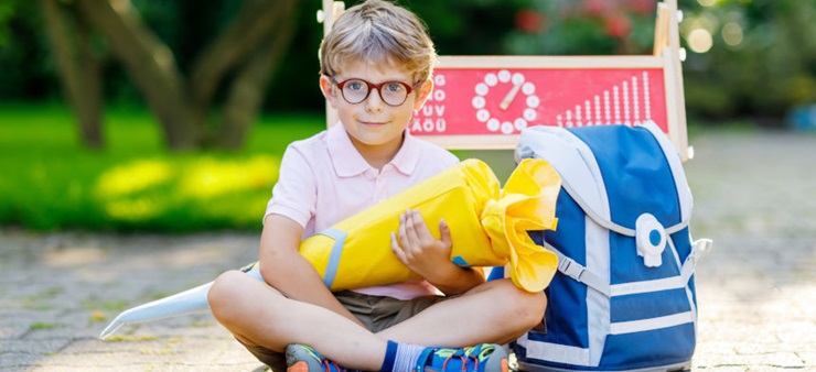 Junge sitzt auf dem Boden mit einer Schultüte in der Hand und Schulranzen.