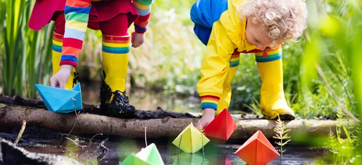 Kinder setzen Papierboote in einen Fluss.