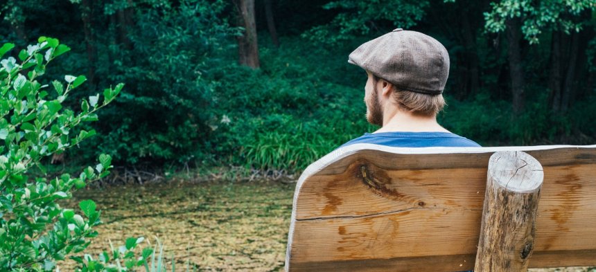 Ein Mann sitzt auf einer Parkbank und schaut in die Natur.