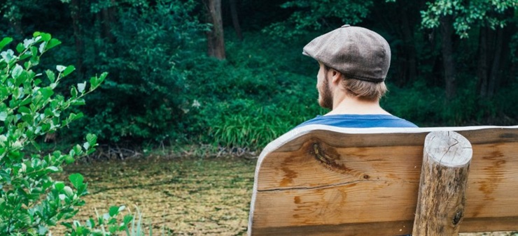 Ein Mann sitzt auf einer Parkbank und schaut in die Natur.