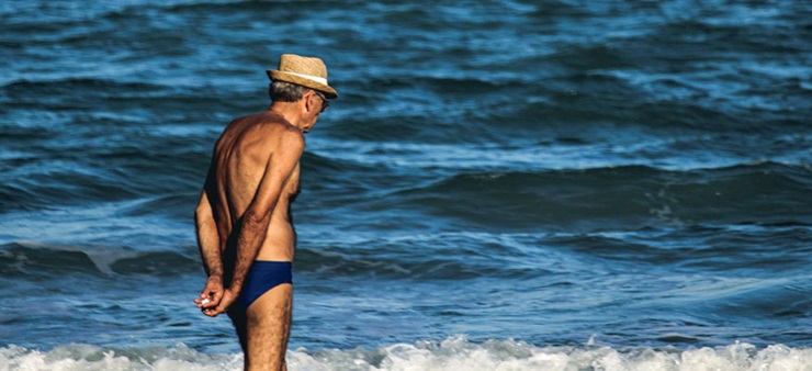 Ein älterer Mann in Badehose steht am Strand