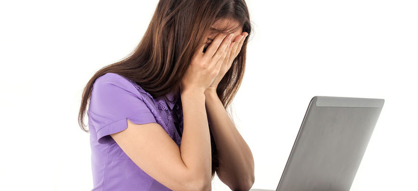 Eine junge Frau sitzt vor dem Computer und hält sich die Hände vor die Augen.