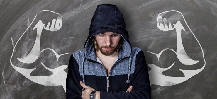 Ein junger Mann steht gedankenverloren vor einer Kreidezeichnung, die ihm muskulöse Arme zu verleihen scheint.