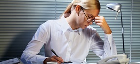 Eine junge Frau am Arbeitsplatz stützt ihren Kopf auf die Hand, da sie offensichtlich angestrengt ist.