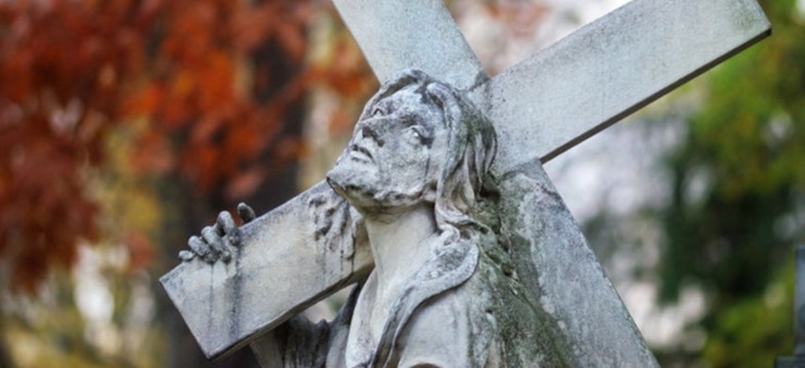 Eine Jesusstatue trägt ein Kreuz über der Schulter und schaut in den Himmel.