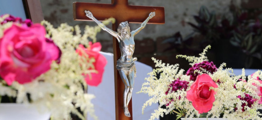 Rosa Rosen umrahmen ein Jesuskreuz.
