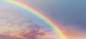 Ein Regenbogen vor pastellfarbenen Wolken in der Dämmerung.