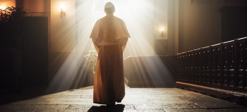 Der Papst schreitet durch eine Kirche in Richtung eines Fensters, aus dem weißes Licht strahlt.