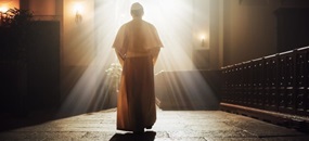 Der Papst schreitet durch eine Kirche in Richtung eines Fensters, aus dem weißes Licht strahlt.