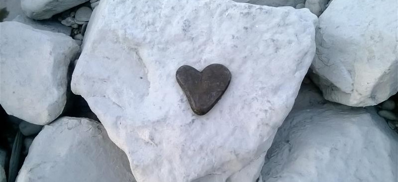 Auf einem großen, weißen Steinbrocken liegt ein kleiner herzförmiger, schwarzer Stein.