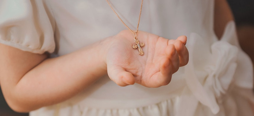 Mädchen im weißen Kleid hält das Kreuz einer Kette in der Hand.