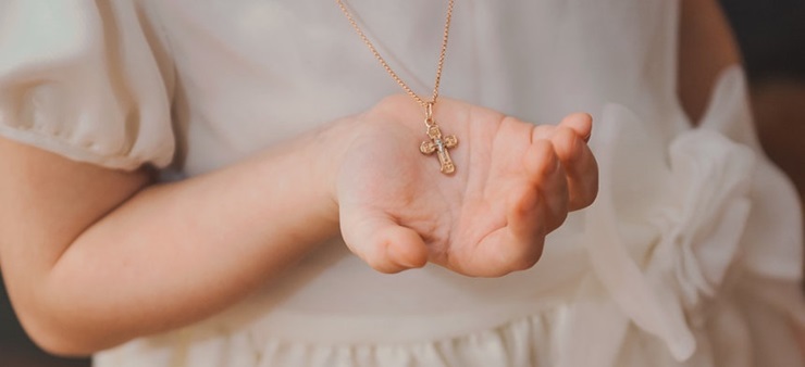 Mädchen im weißen Kleid hält das Kreuz einer Kette in der Hand.