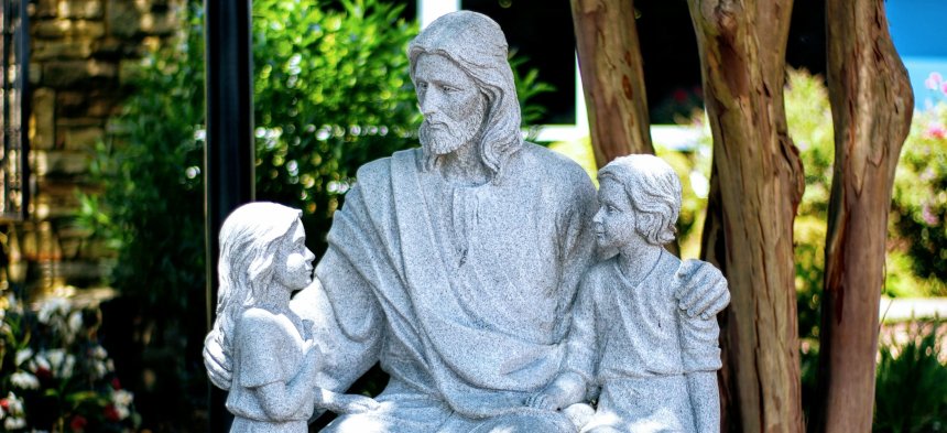 Eine weiße Jesus-Statue legt seine Arme um Kinder-Statuen