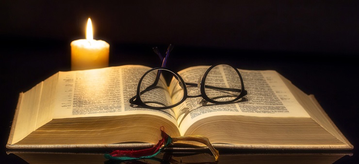 Offene Bibel mit Kerze und Brille, die darauf liegt