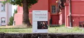 Das Buch "Freundschaft" steht auf einer Mauer, im Hintergrund ist ein rotes Haus