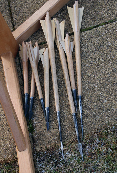 Foto einer Ansammlung von Geschützbolzen mit unterschiedlich langen Schäften und Metallspitzen, auf dem Boden liegend. 