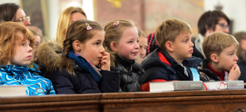 Kinder sitzen in einer Kirchenbank und hören gespannt zu