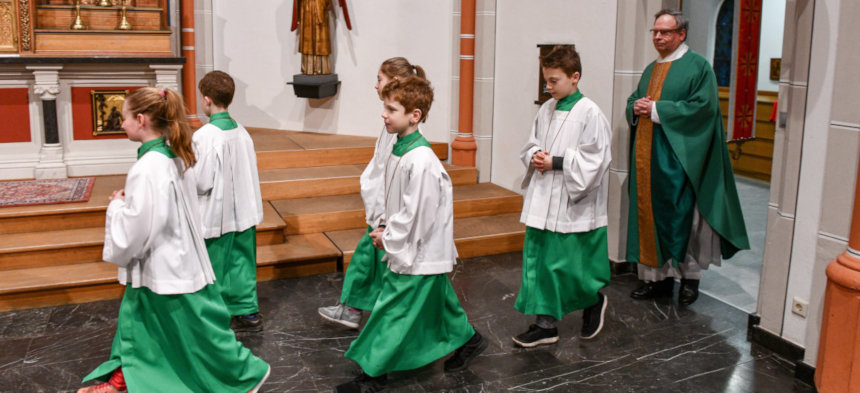 Ministranten ziehen vor dem Priester in die Kirche ein