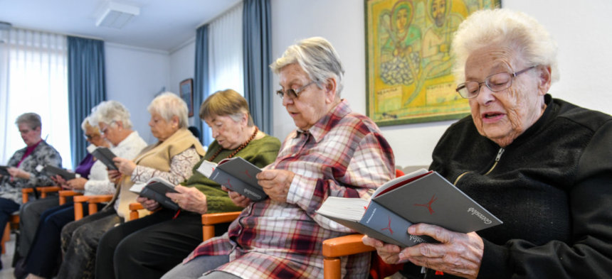 Senioren sitzen in einer Reihe und halten kirchliche Gesangbücher in der Hand