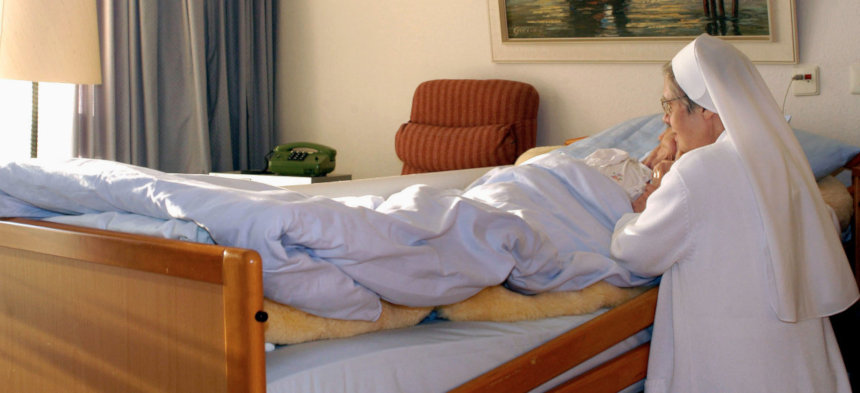 Eine Nonne kniet am Krankenbett eines Menschen und betet 