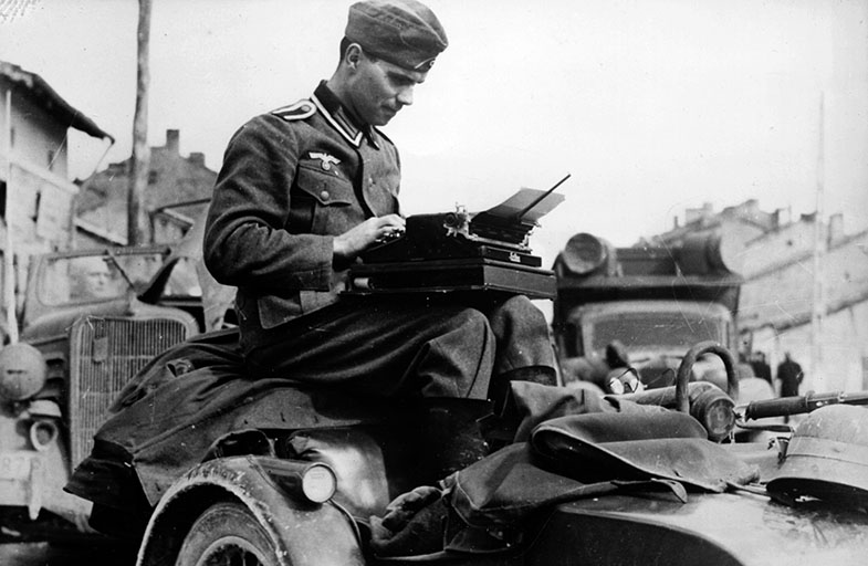 Abb. 4 Kriegsberichter einer Propagandakompanie der deutschen Wehrmacht auf einem Militärfahrzeug beim Schreiben seines Berichtes in Bulgarien, März 1941.