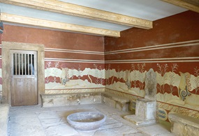 Abb. 2 Eine Seitenansicht des Thronraums im Palast von Knossos, links eine Tür, rechts der Thron, an den Wänden die rekonstruierten Wandmalereien in erdigem Rot mit liegenden Greifen.