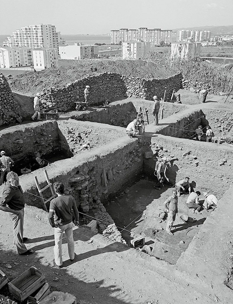 Abb. 4 Moderne trifft Antike. Ausgrabungen in der phönizischen Siedlung Toscanos vor den Wohnblöcken der südspanischen Stadt Vélez bei Málaga. Mehrere Arbeiter graben in einem Raum, um sie herum erheben sich die erhaltenen Mauern des Raums, eine Leiter lehnt an der Seite.