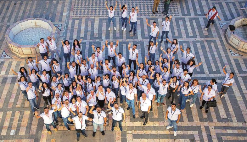 Junge Menschen in weißen Hemden winken von einem Platz in die .erhöht stehende Kamera. Sie sind Teil einer Aktion des päpstlichen Hilfswerks „Kirche in Not“, bei der in Damaskus Fördermittel an Unternehmer verteilt werden.